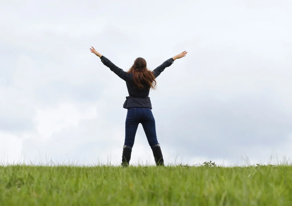 Frau mit ausgebreiteten Armen in der Natur symbolisiert Integration von Arbeit und Leben als Ganzes