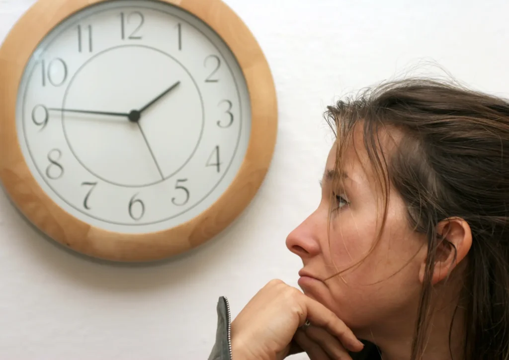 Frau sitzt allein, nachdenklich mit Uhr an der Wand