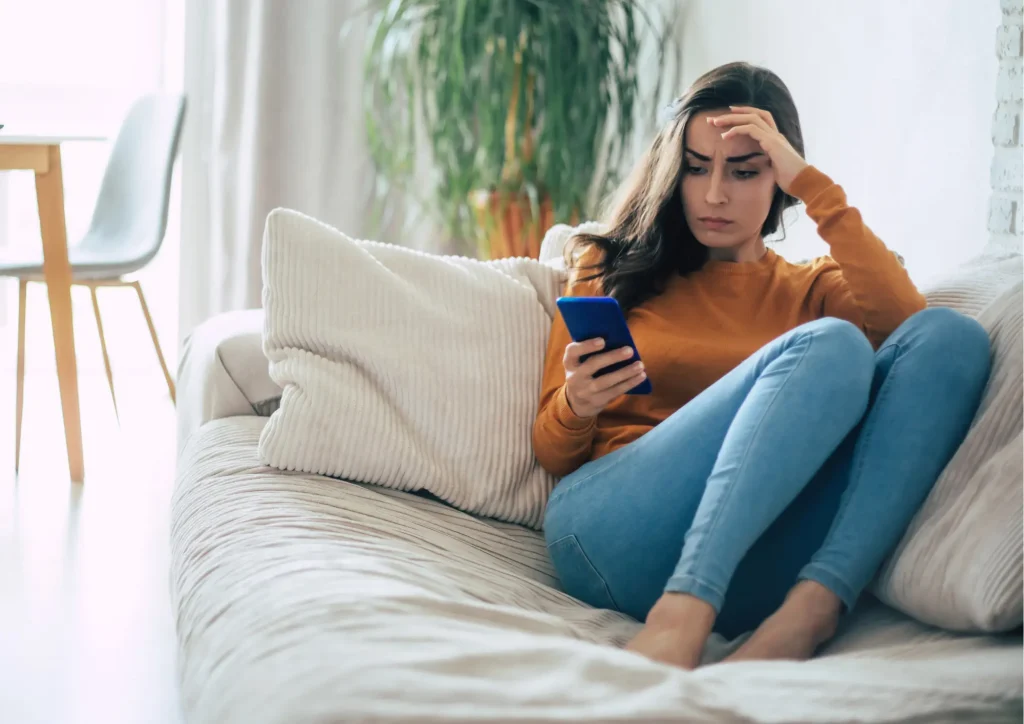 Frau sitzt nachdenklich mit Smartphone am Fenster